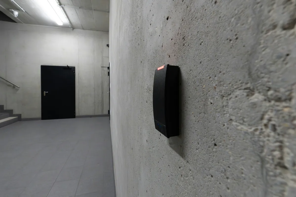 Black badge reader with a red status light mounted on a concrete corridor wall